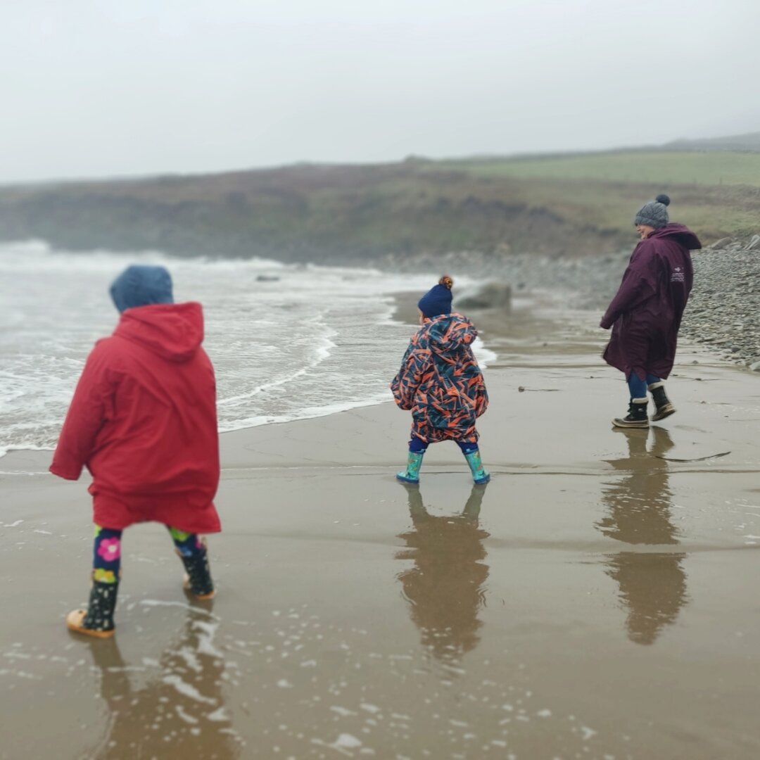 An adult and two children on a beach close to the sea, dressed for rainy and cold weather