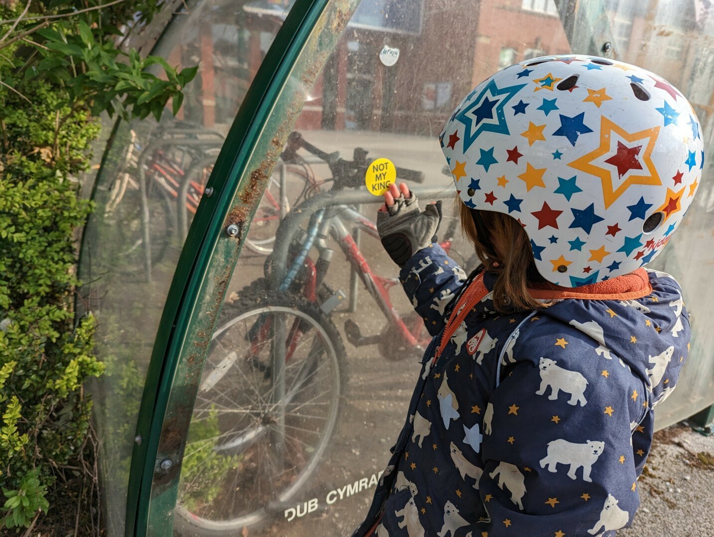 A young boy in a bicycle helmet touches a sticker that says 'Not my King'