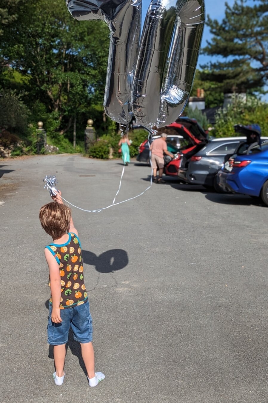 A boy holding two helium balloons, one is a 7 and the other is a zero