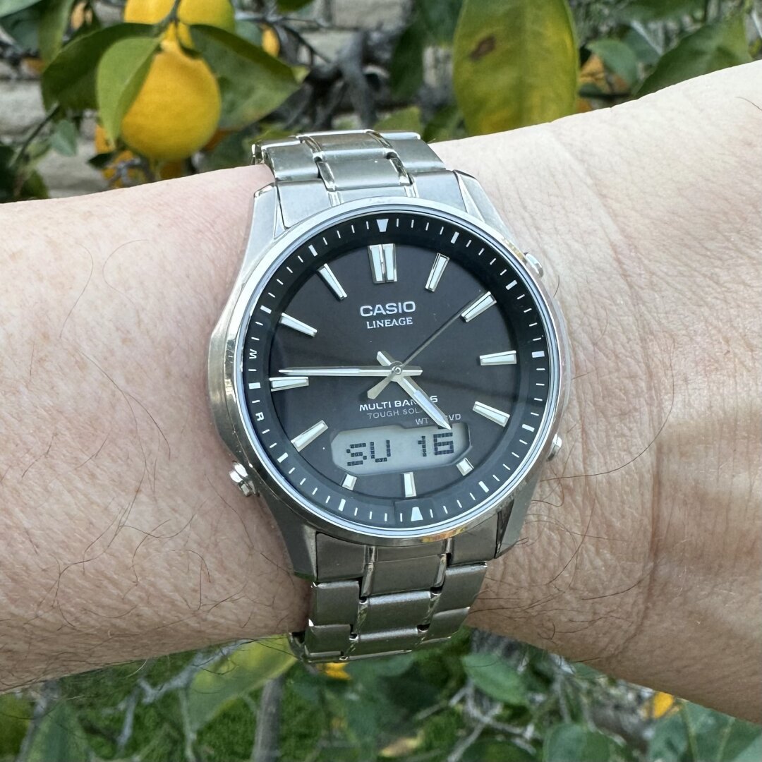 Watch with brushed and polished titanium case, gray-brown sunburst dial with faceted and polished baton hands and baton indices, double index at 12, digital display above the 6:00 index, and pushers at the 2:00, 4:00, and 8:00 positions. On a brushed titanium 3-link bracelet with female end links and polishing on the outer edge of the center links.