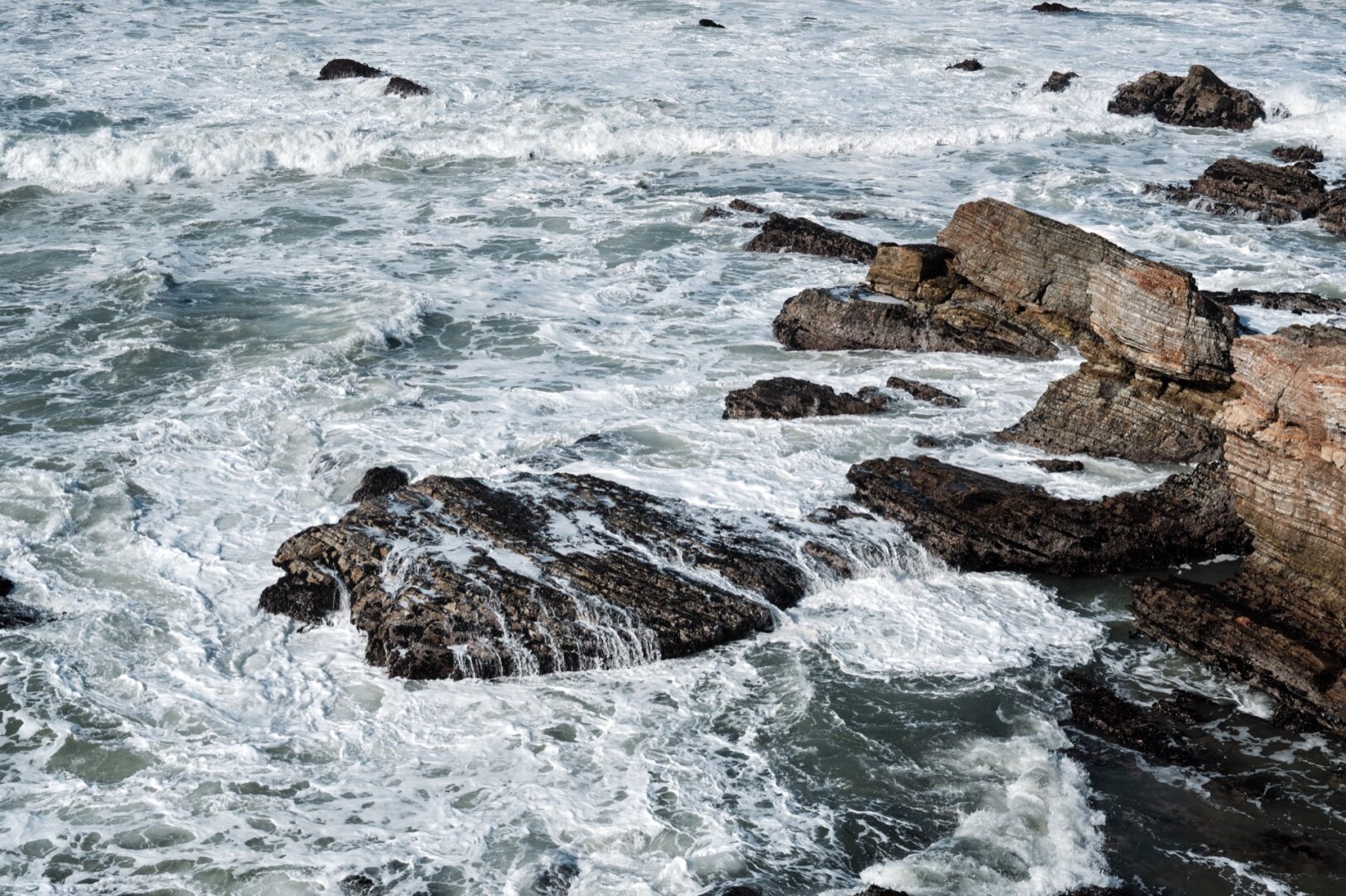 photograph of ocean waves breaking over large rocks in the water