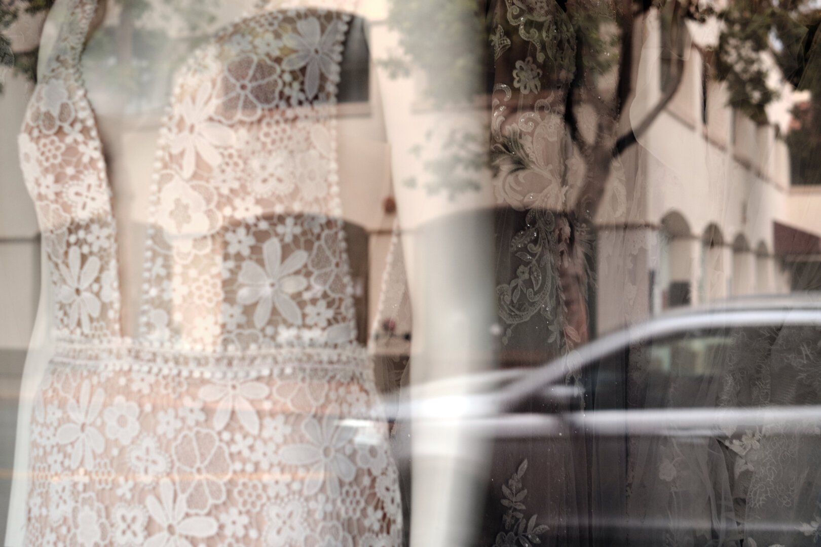 Photo of mannequin in a shop window wearing a wedding dress with reflections of cars in the street and buildings.