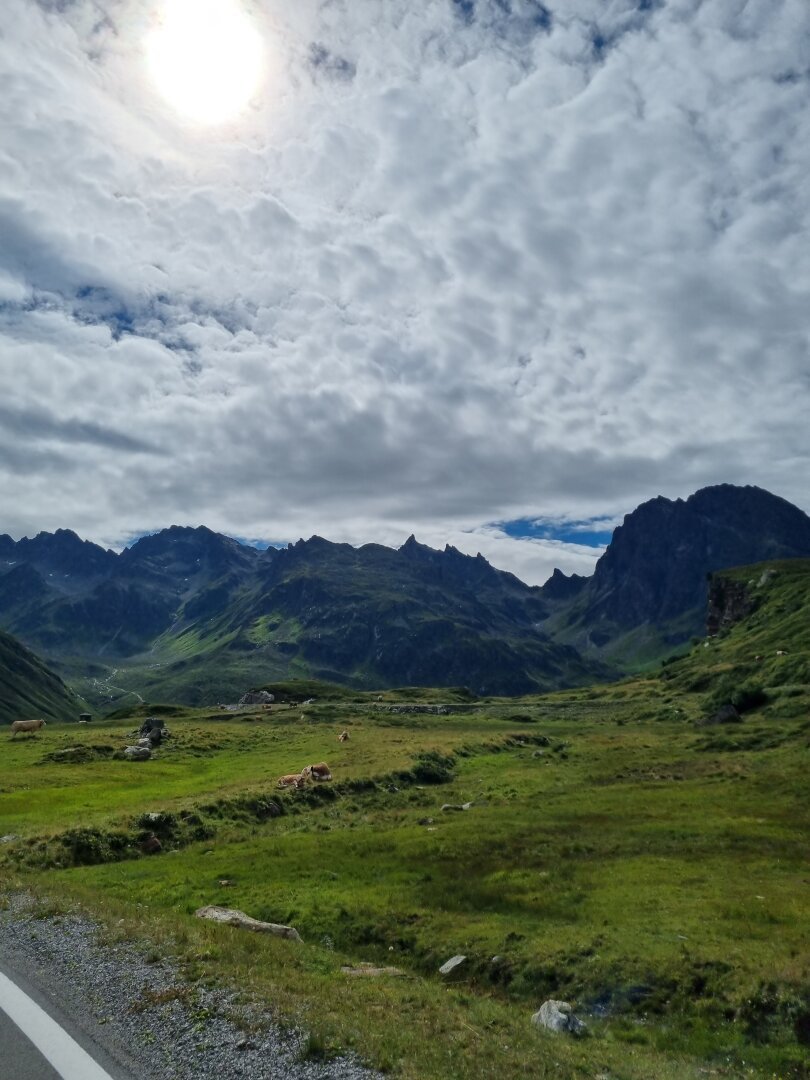 Groen weiland met erachter hoge bergen en erboven wolken met zon.