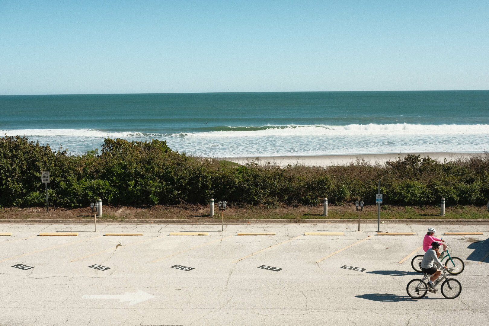 A photo of 2 bicyclist cycling through a drive way with the ocean in the background.