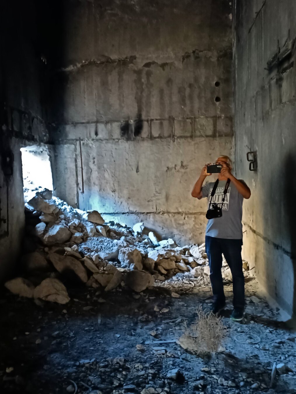 A man takes a photo from inside a nuclear bunker. Rubble has fallen in through an opening in the wall behind him.