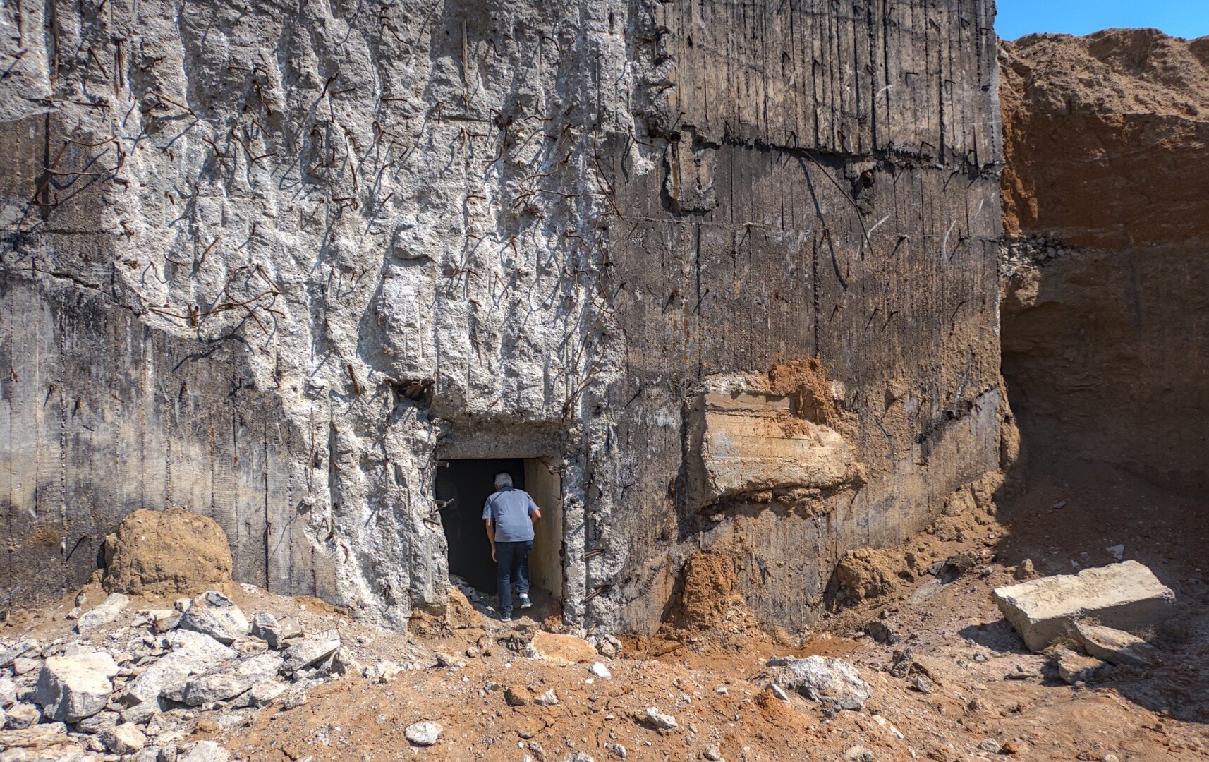 A man stoops down to enter a small entrance in a large concrete structure