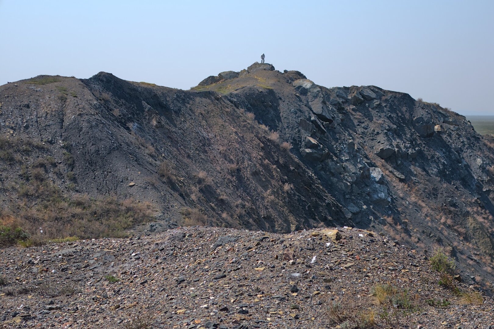 A small figure in a HAZMAT suit stands atop a huge mound of earth forming  part of the crater that is now the Atomic Lake