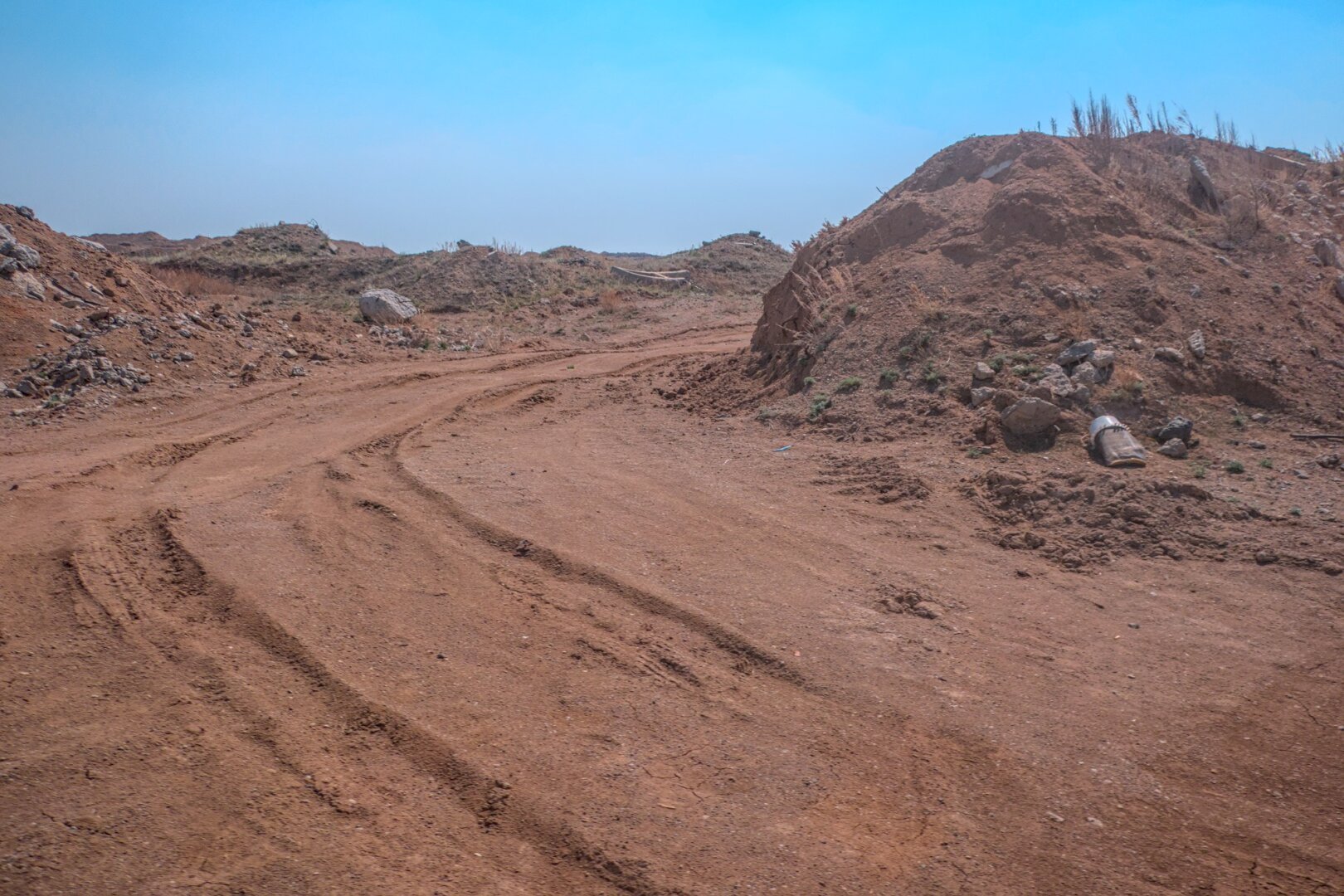 A dust dirt road winds it's way around a mound of earth. The reddish soil contrasts starkly with the famous blue Kazakh sky.