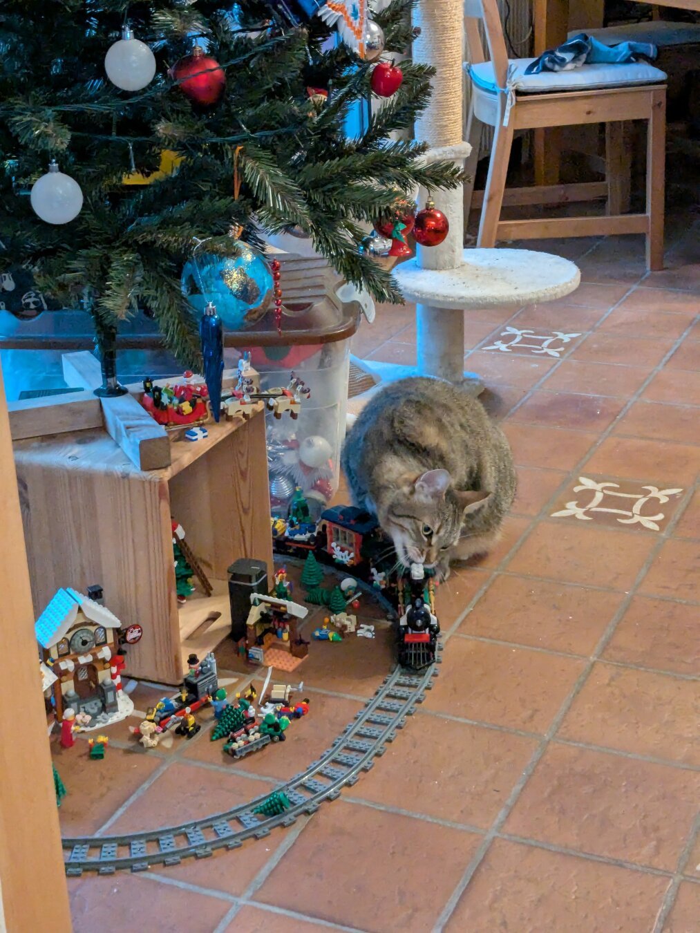 A cat munching on the chimney of a Christmas Lego train under a Christmas tree.