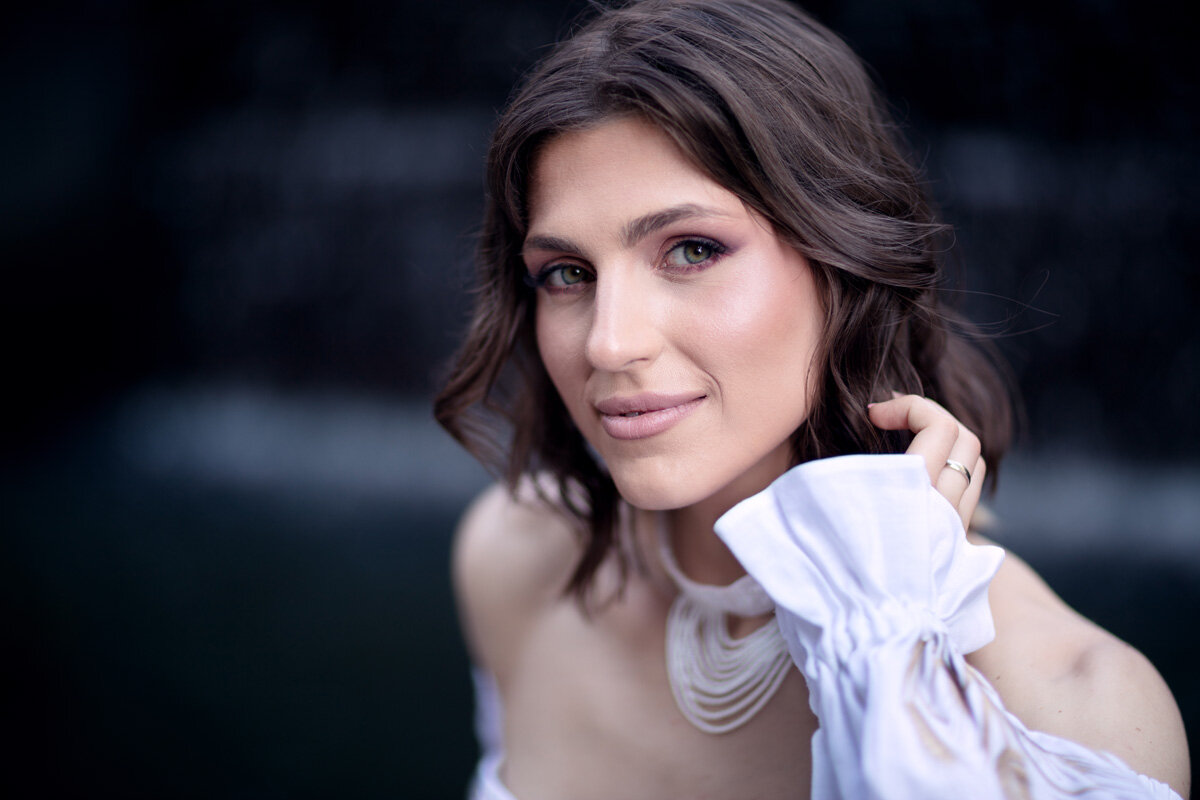 Close up portrait of a young Ukrainian women. The dark black background contrasts with her skin tone and white outfit.
