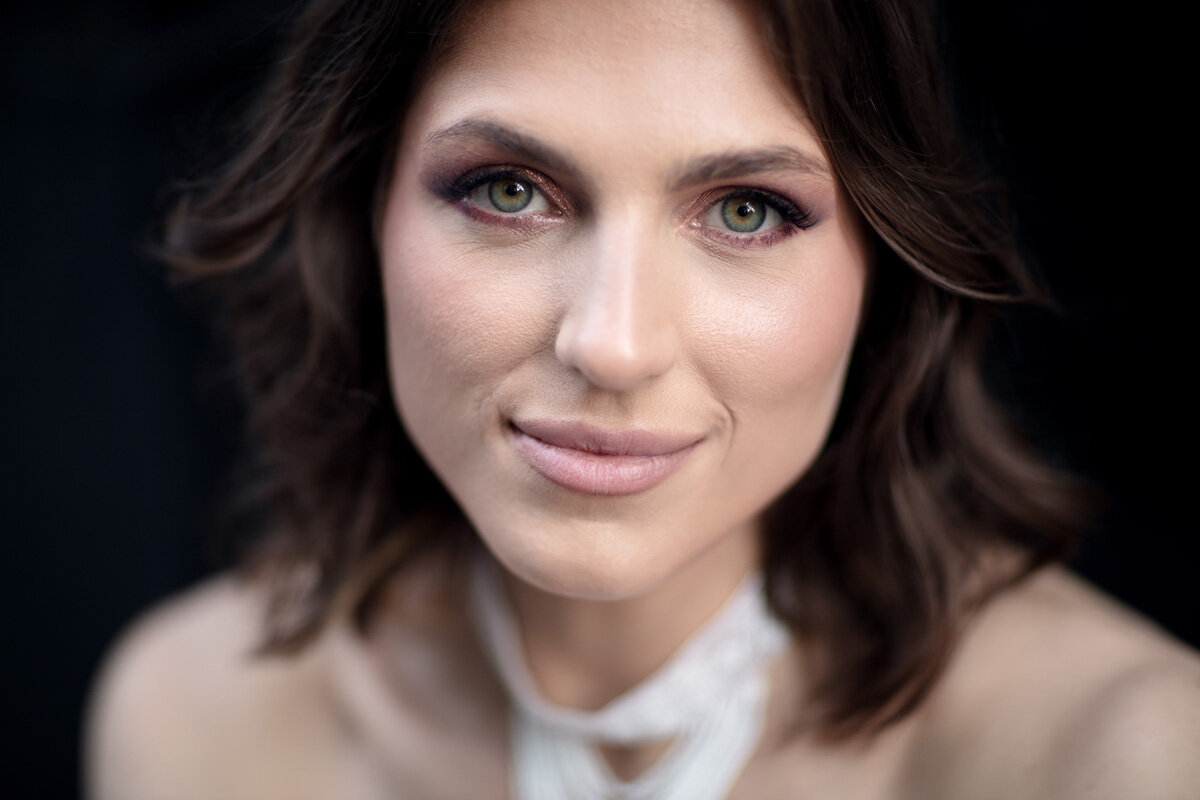Close up portrait of a young Ukrainian woman. Her green eyes and pale skin tone contrasts with the black background.