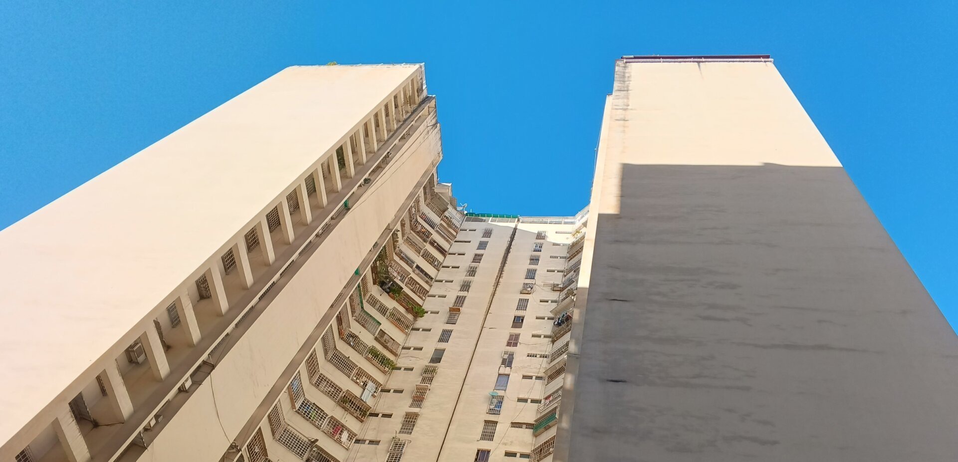 A photo of two very tall apartment buildings under a clear blue sky, seen from below.