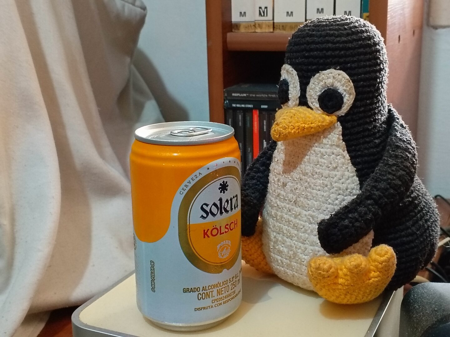 A photo of a Tux plushie looking at a can of beer. The plushie and beer are atop a Mac Mini computer.