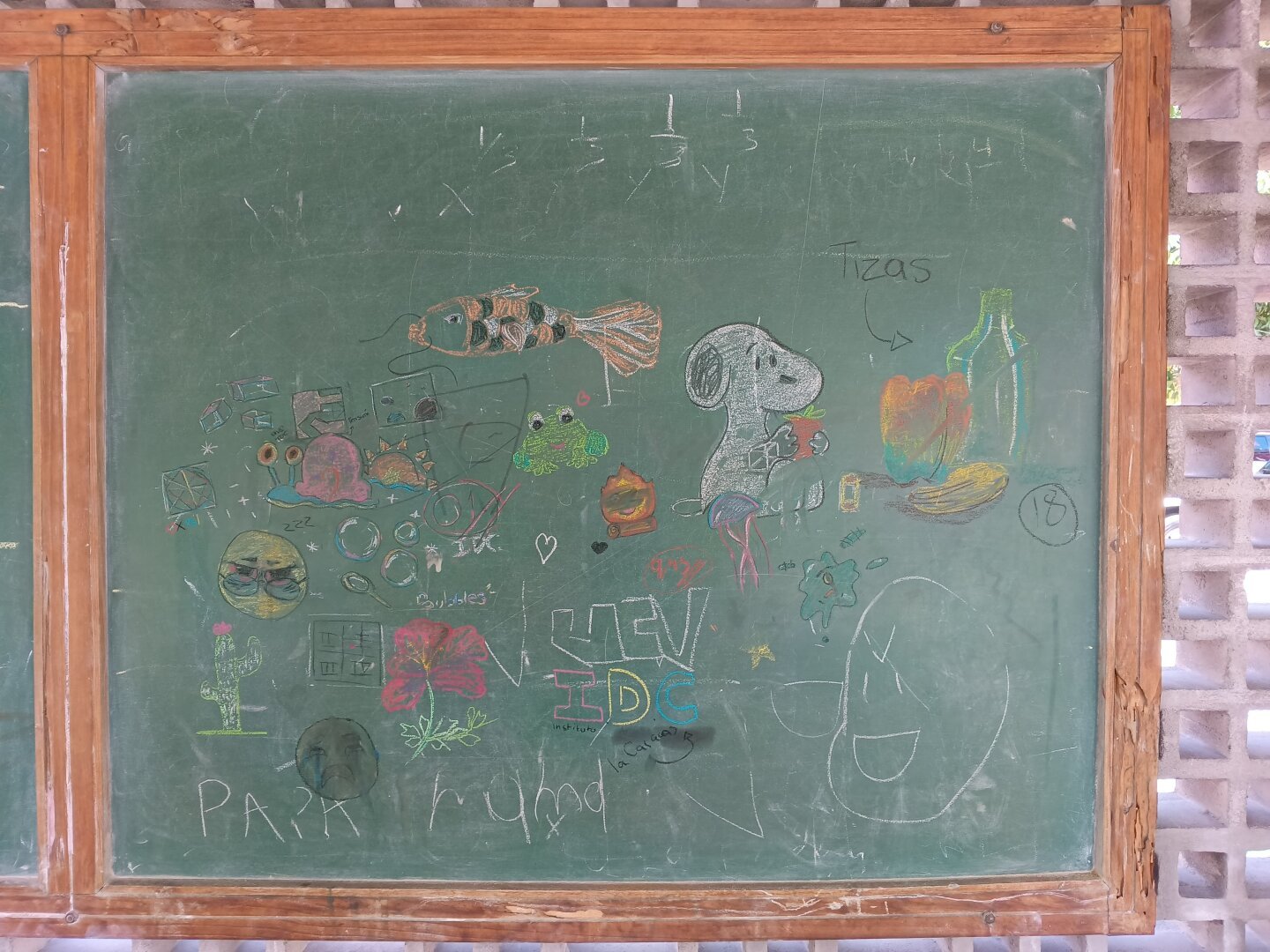 A photo of a green blackboard with chalk drawings on it, including a Snoopy, a frog, Gary the snail, a fish and an emoji.