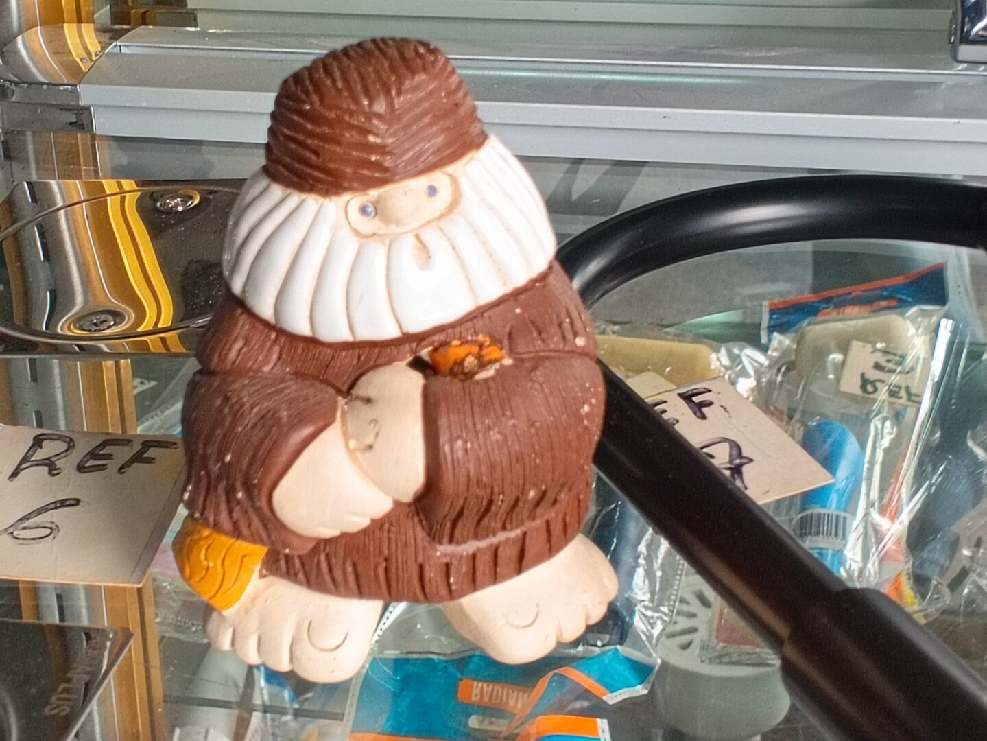 A photo of a small sculpture of a gnome-like figure with brown robes and hat, an orange pouch and a white bushy beard.