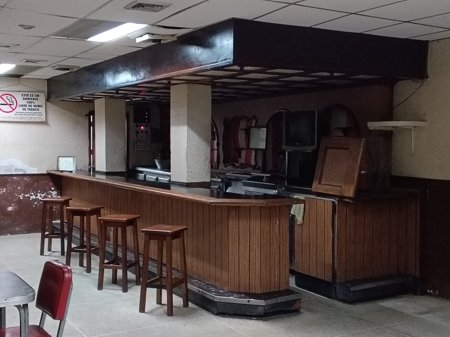 A photo of an empty bar counter with four wooden chairs in front.