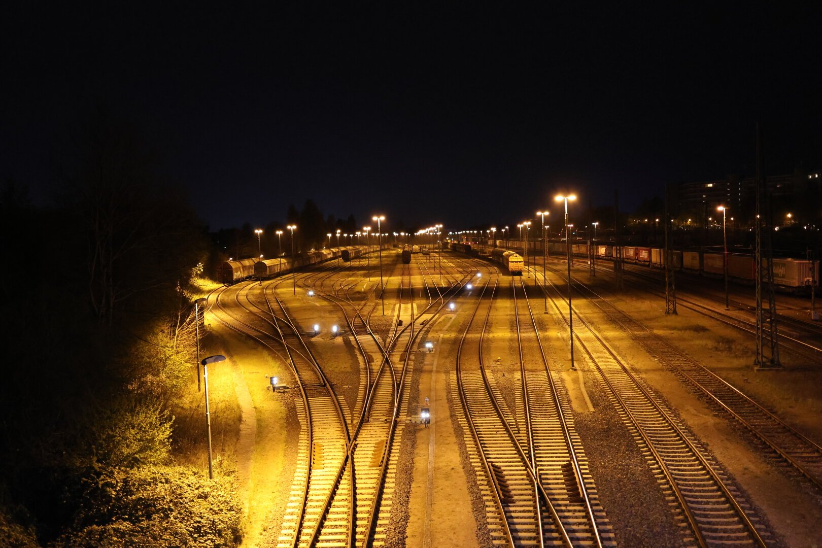 Blick über die Bahngleise vor dem Lübecker Bahnhof bei Nacht. Es stehen im Hintergrund diverse Waggons. Es ist Nacht. Die Szenerie ist gelblich beleuchtet.