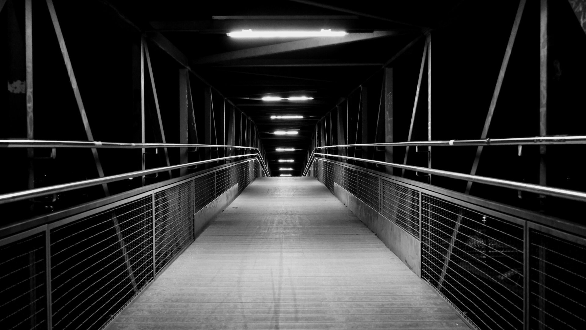 Graustufen. Menschenleere Fußgängerbrücke bei Nacht. Starke Symmetrie des Geländers links und rechts.