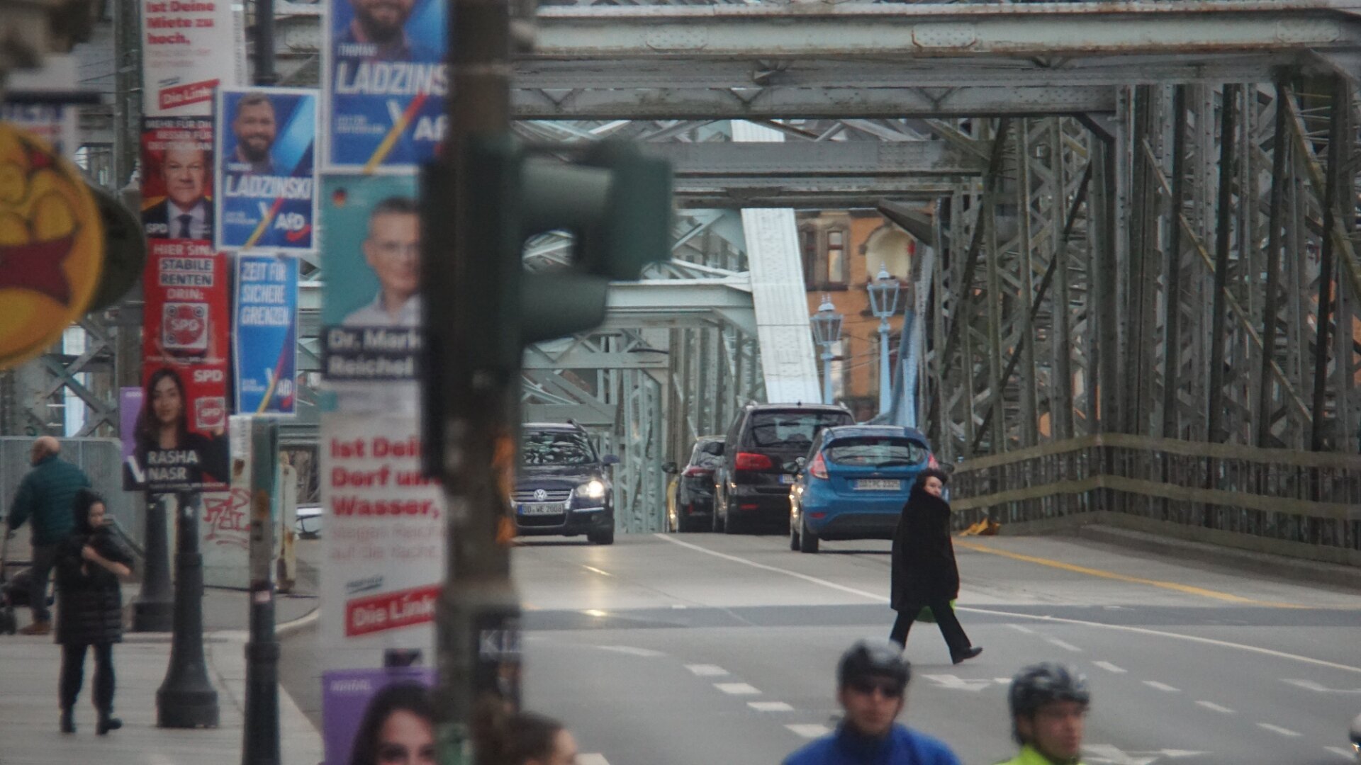 Blick längs auf's blaue Wunder, alles voller hässlicher Wahlplakate

paar PKW, Radfahrer und Fußgänger