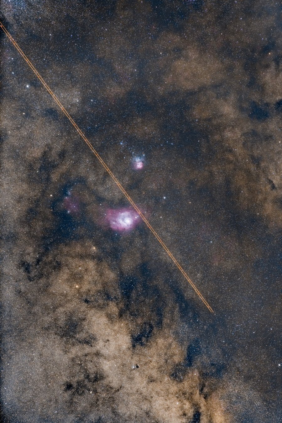Image of the night sky. In the center is the Lagoon Nebula and at the top the Trifid Nebula. The lights of an airplane have drawn two perfect lines from the top left to the bottom right. You can appreciate the colors of the Milky Way.