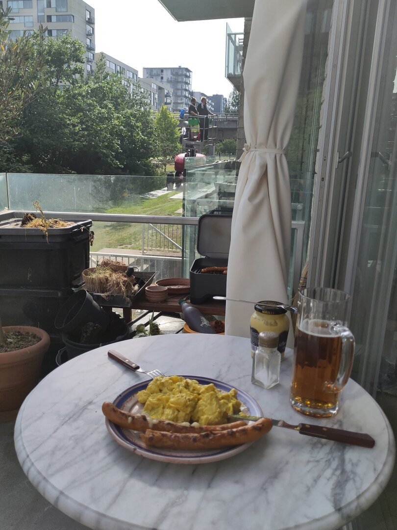 Billede af en middagstallerken og et glas øl på et cafebord. To mænd på en lift i baggrunden.