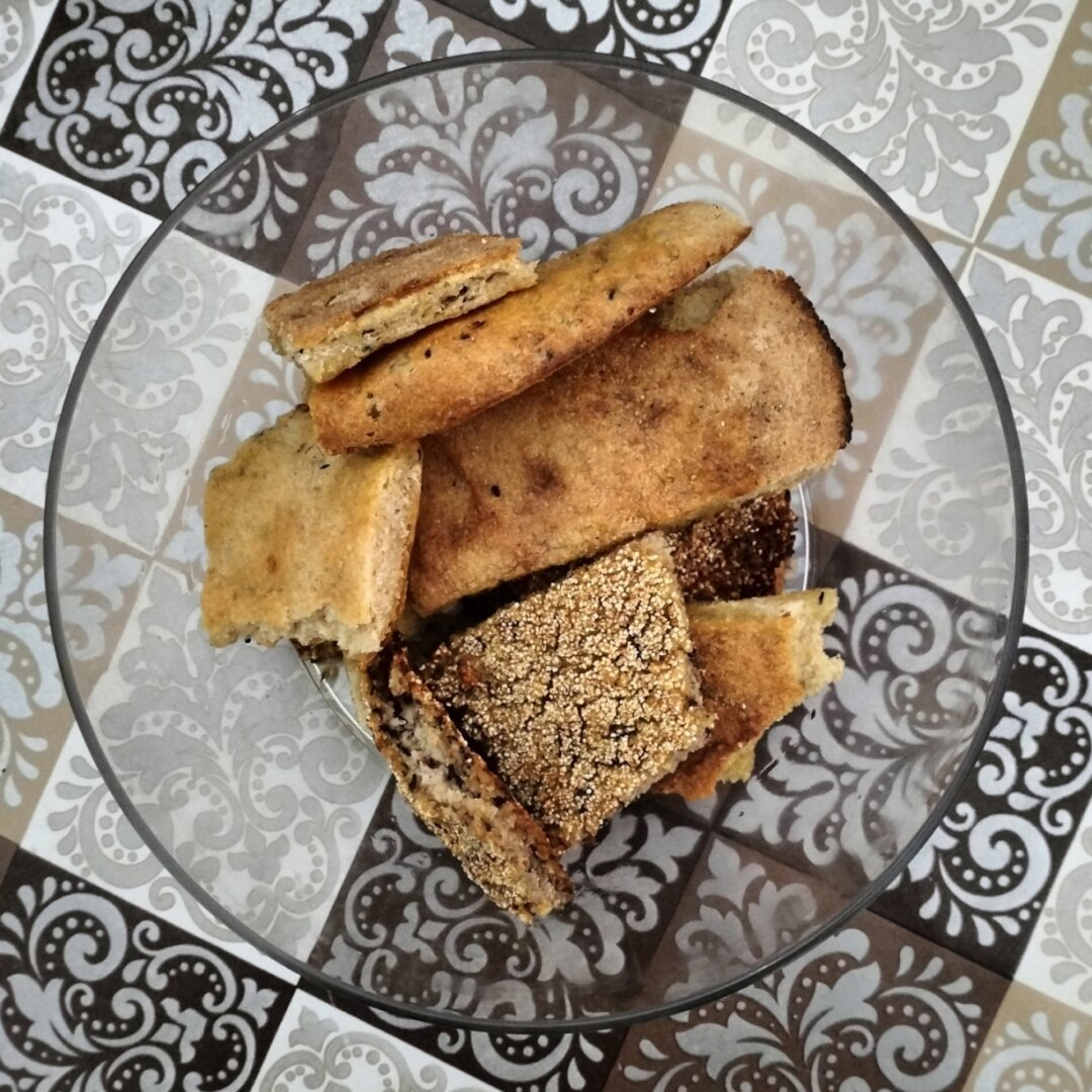 Des morceaux de pain artisanal tunisien (Tabouna et Kesra) imprégnés d'huile d'olive dans un bol transparent.