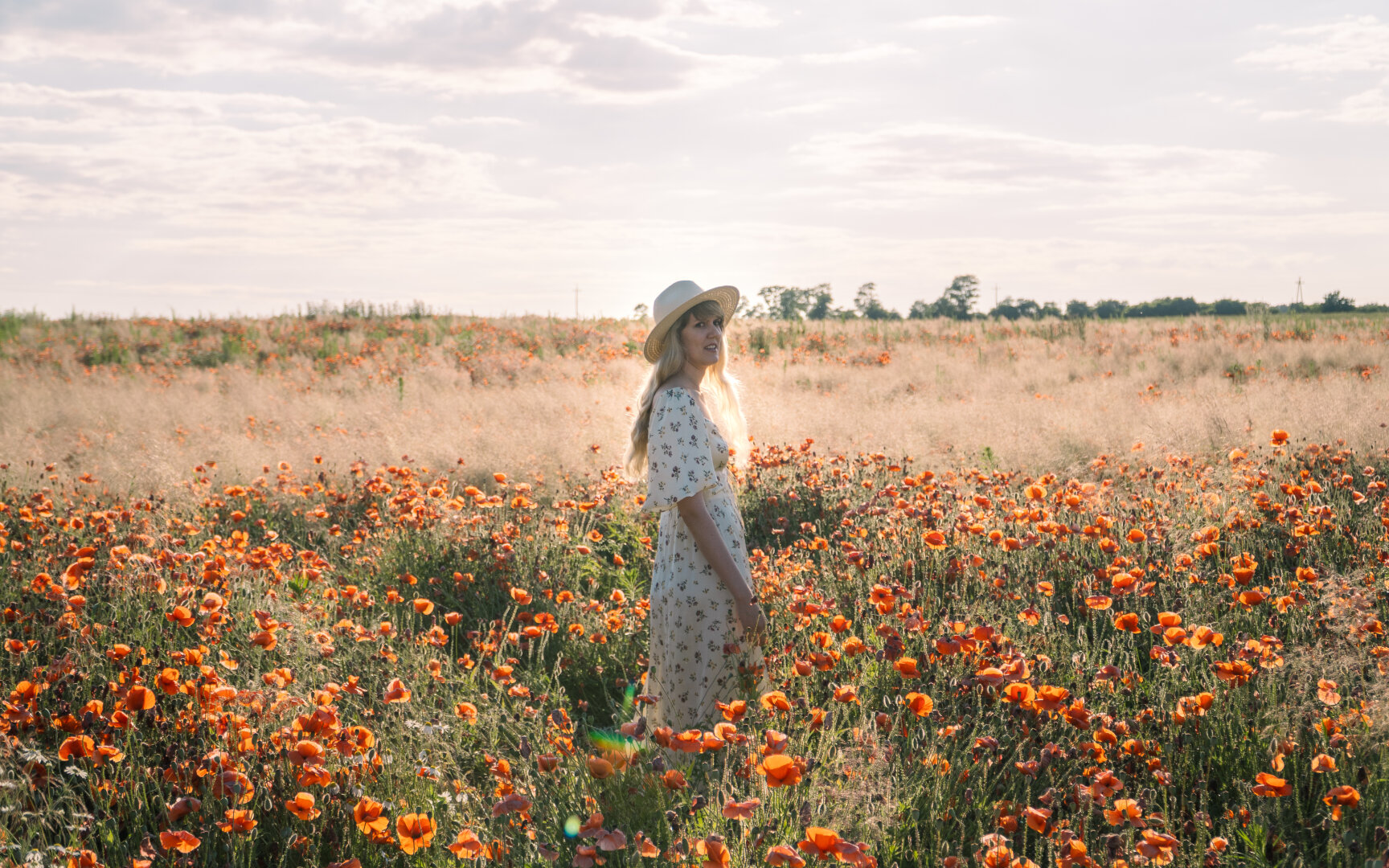 A girl in a light-colored dress and a hat is standing in a field of poppies