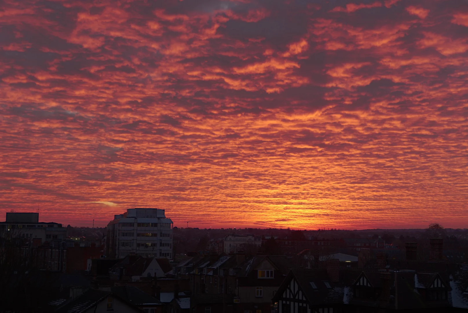 Sunrise over Lewisham. The sun is rising just over the horizon and the clouds have a very strong red colour as if they were on fire. On the foreground there are a few buildings.