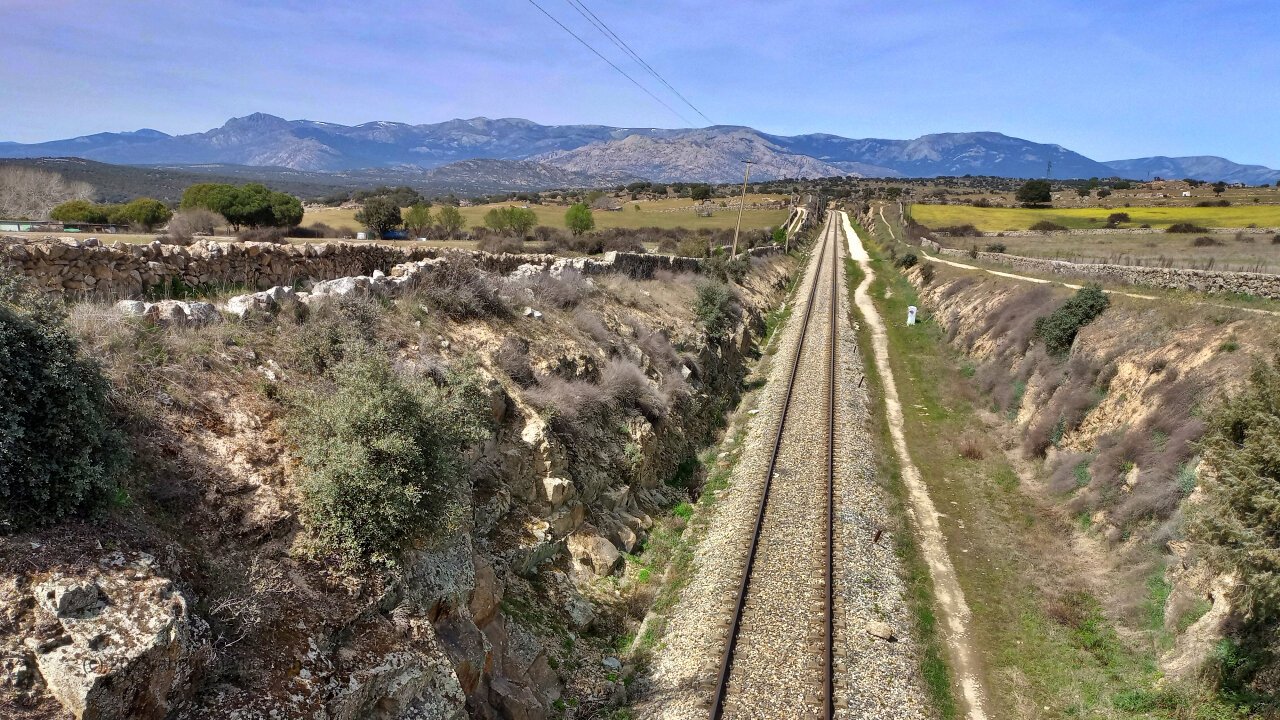 Une voie ferrée au milieu d'un paysage aride d'Espagne avec des montagnes au fond.