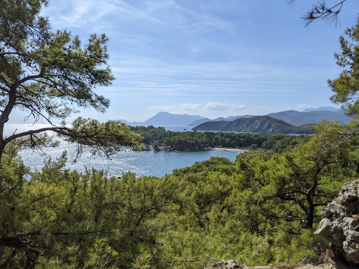 View from the top of the hill, a lot of green plants and trees, the sea, the mountains, a very green peninsula and blue sky.