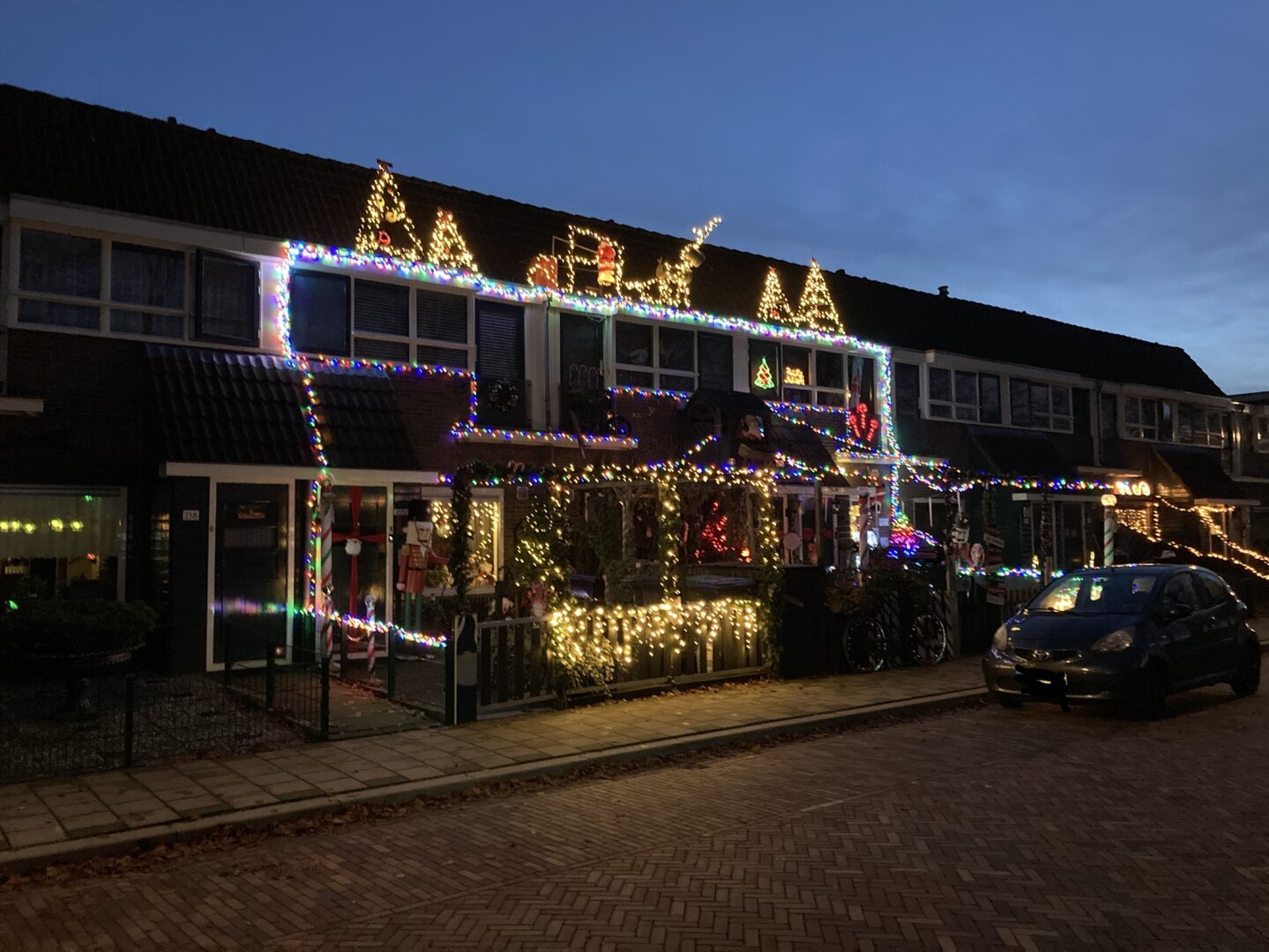 A street in darkness with christmas lights and a car parked in front.