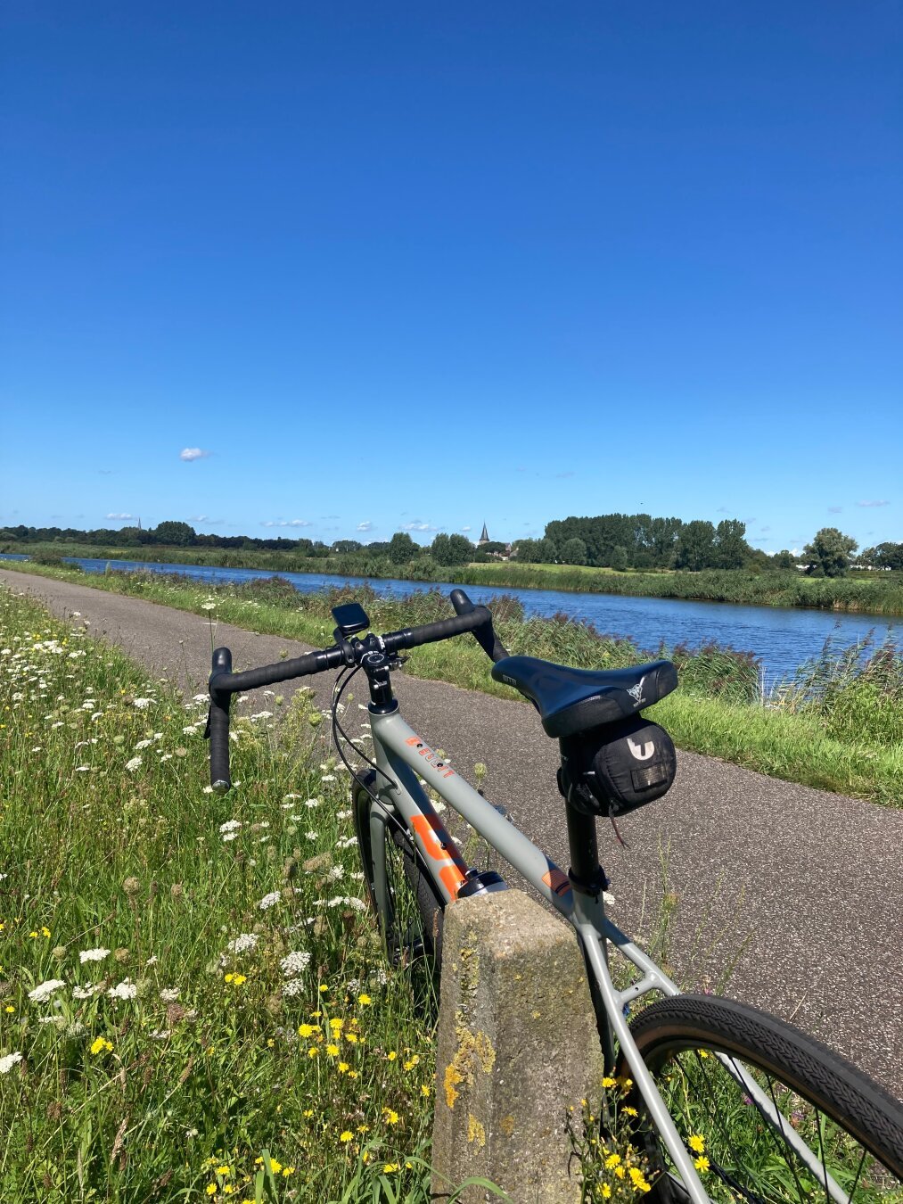 A gravelbike parked next to the cyclepath. In the background is a river under the blue sky