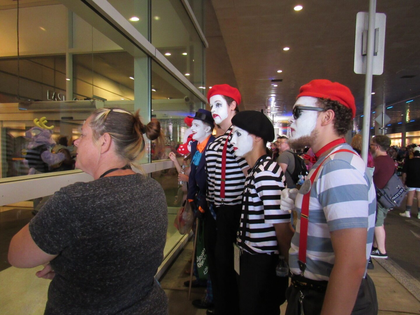 A cosplayer doing Joker from Batman leans on his cane as he checks out furries in Anthrocon's fursuit parade. He has three henchmen mimes with them, and they all look at the parade perplexed. In front of them, a woman continues to watch the parade, and next to them a red dog fursuiter looks on at the parade as well.