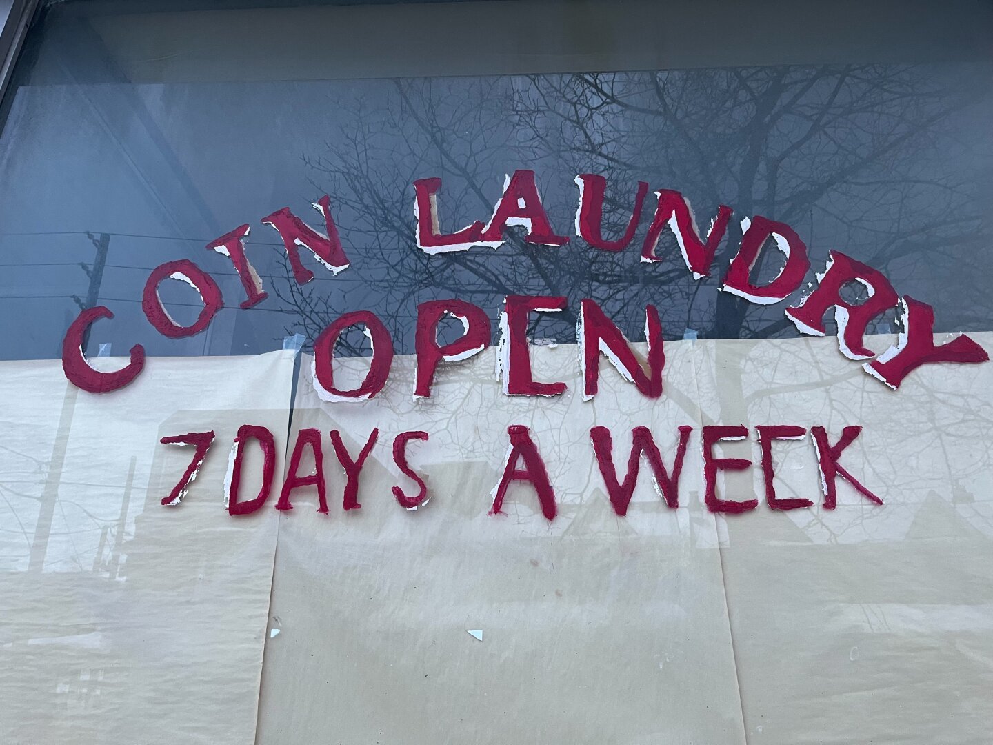 Closed coin laundry mat sign. With reflections of a tree lined street.