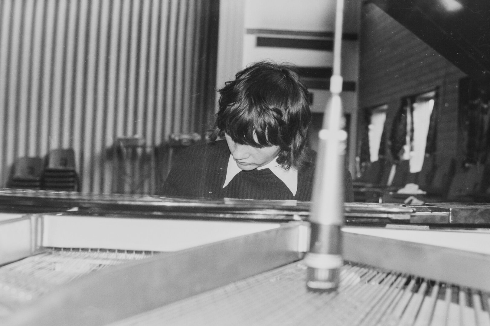 Photo of a young man playing agrand piano. Shot across the bed of strings. A microphone hangs just above the piano strings.