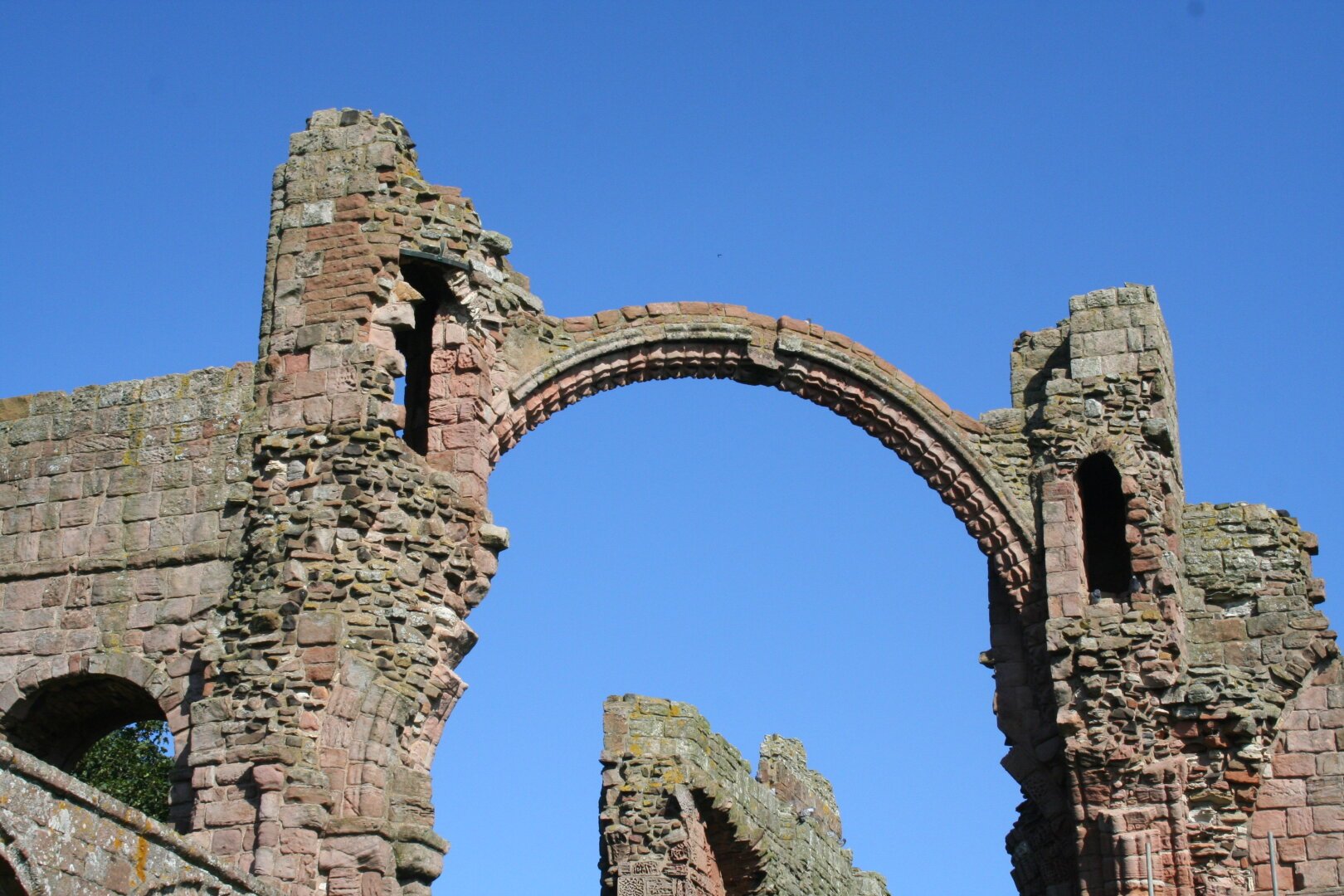 a ruined abbey made from sandstone with a single stone arch linking two stone piers, high up with a blue sky behind.