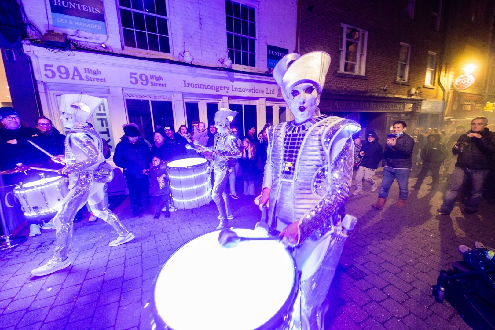 Drummers with LEDs in their drums and costumes parade through a street at night