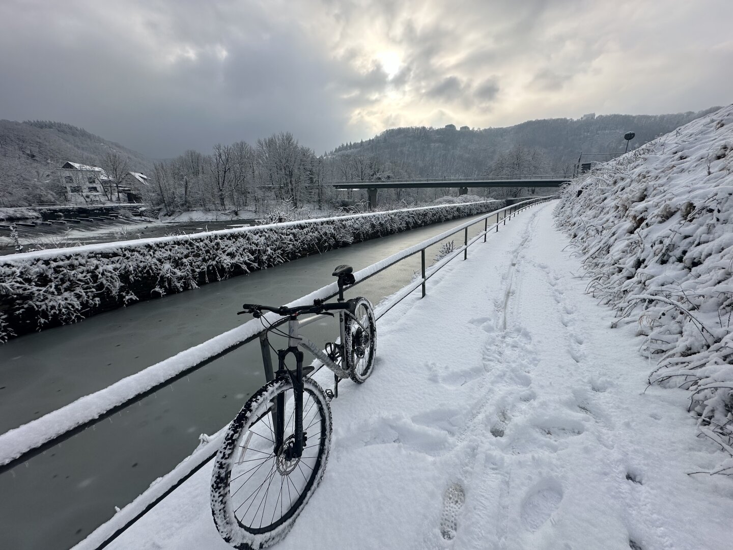 River Lahn in the snow in the sun. In the background a bridge over the rivers, in the foreground a mountaimbike