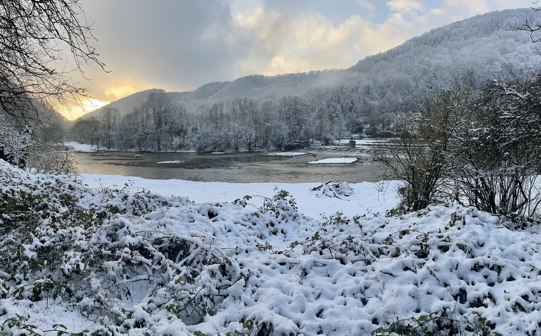 A snow covered landscape with a river and the sunset in the background