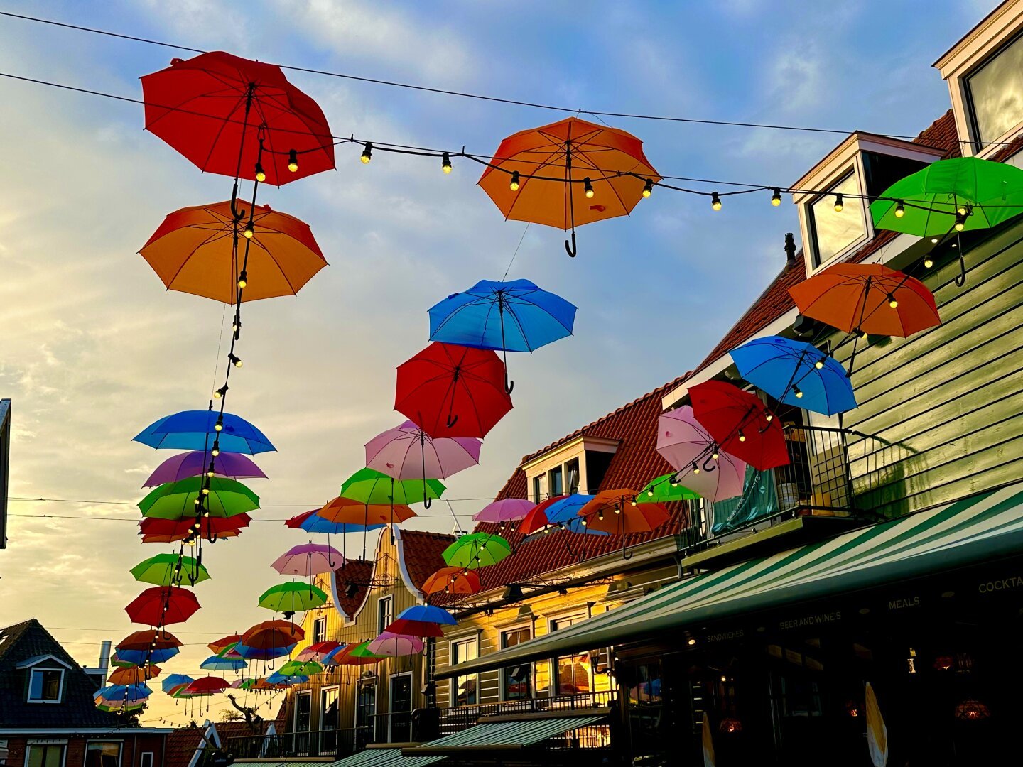 Colorful umbrellas hang over a street and are lit by the sunset