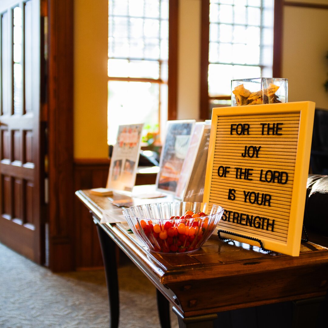 A picture of a table in the foreground with a bowl of cherry tomatoes and a board saying “For the joy of the Lord is your Strength”