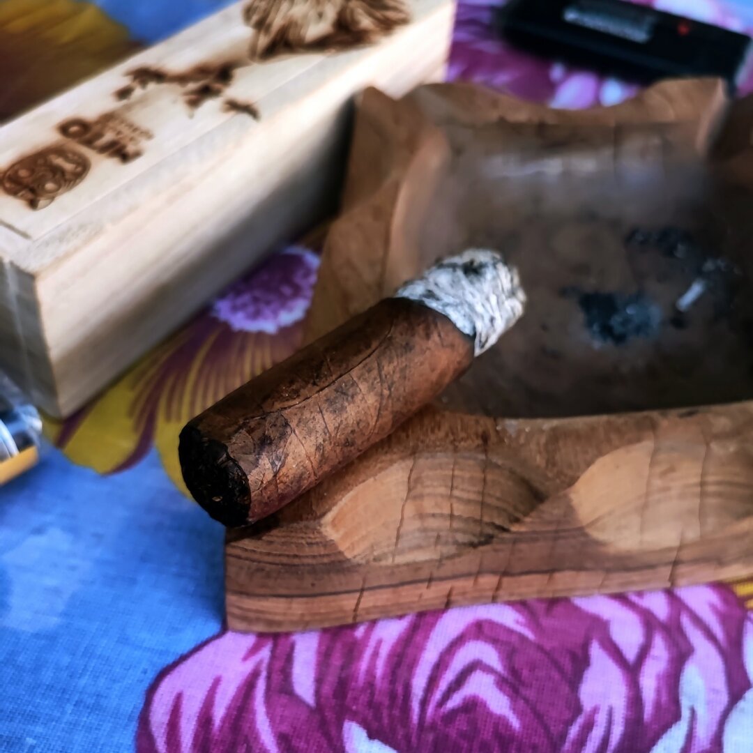 Cigar burning, resting on an ashtray, beside another cigar box