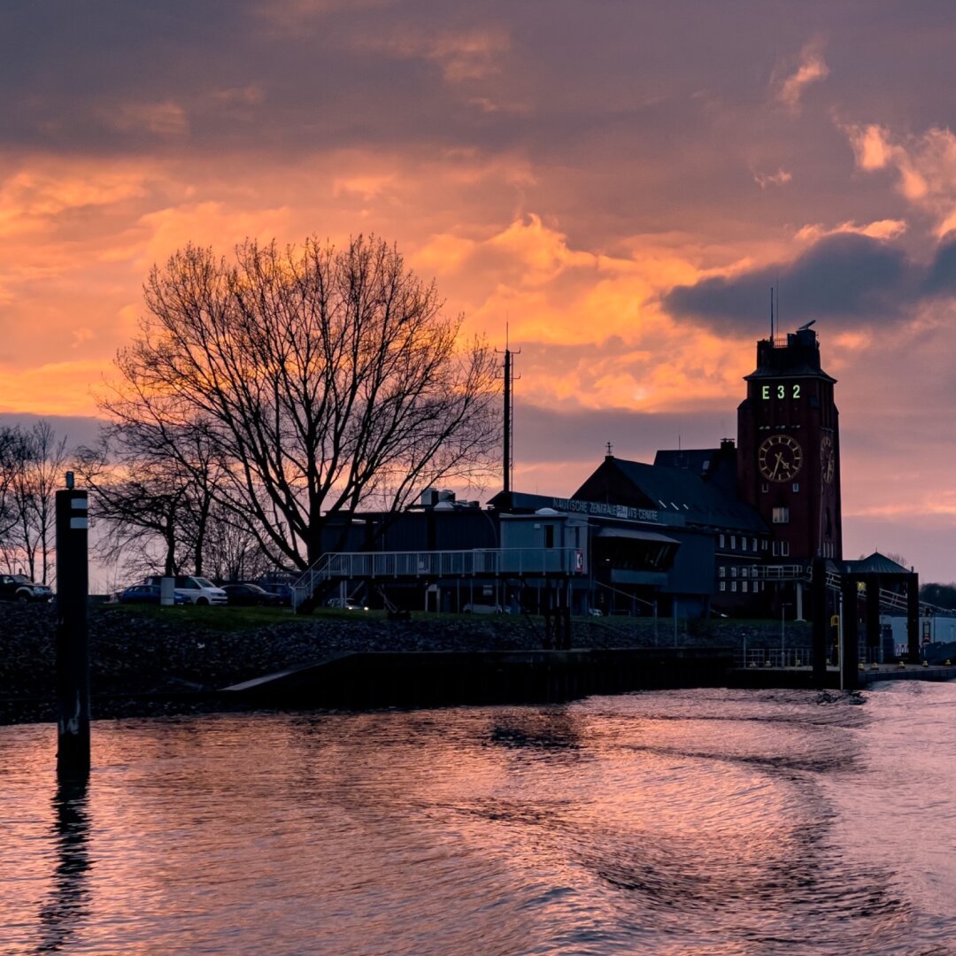 orange farbender Himmel im Hintergrund, davor das Lotsenhaus mit Anleger. Die Elbe in der sich der orangene Himmel spiegelt.