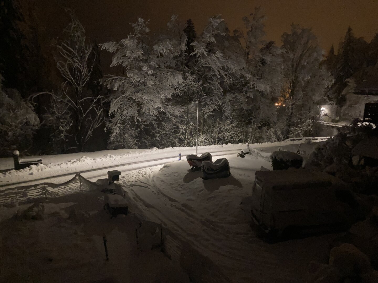 It’s night and dark. A couple streetlights shows that the street and nearby trees and garden are covered in 10cm of fresh snow.