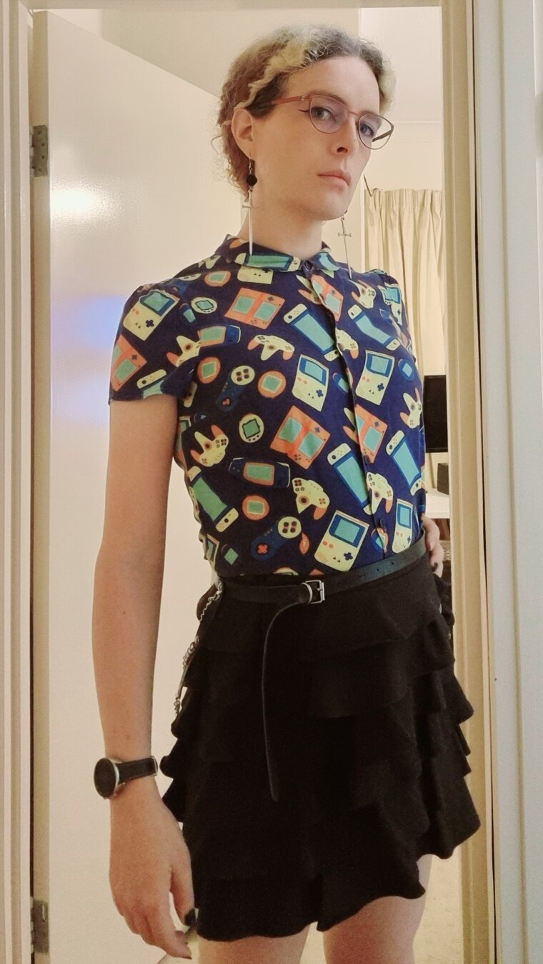 Woman wearing a blue games themed blouse, layered skirt and chain belt