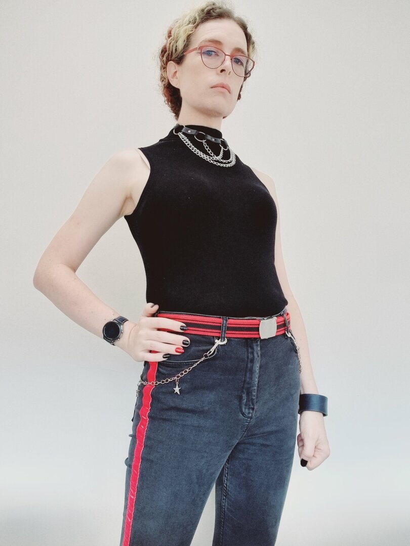 Woman in black tank top,  jeans. Red/black theme with chains. Red glasses