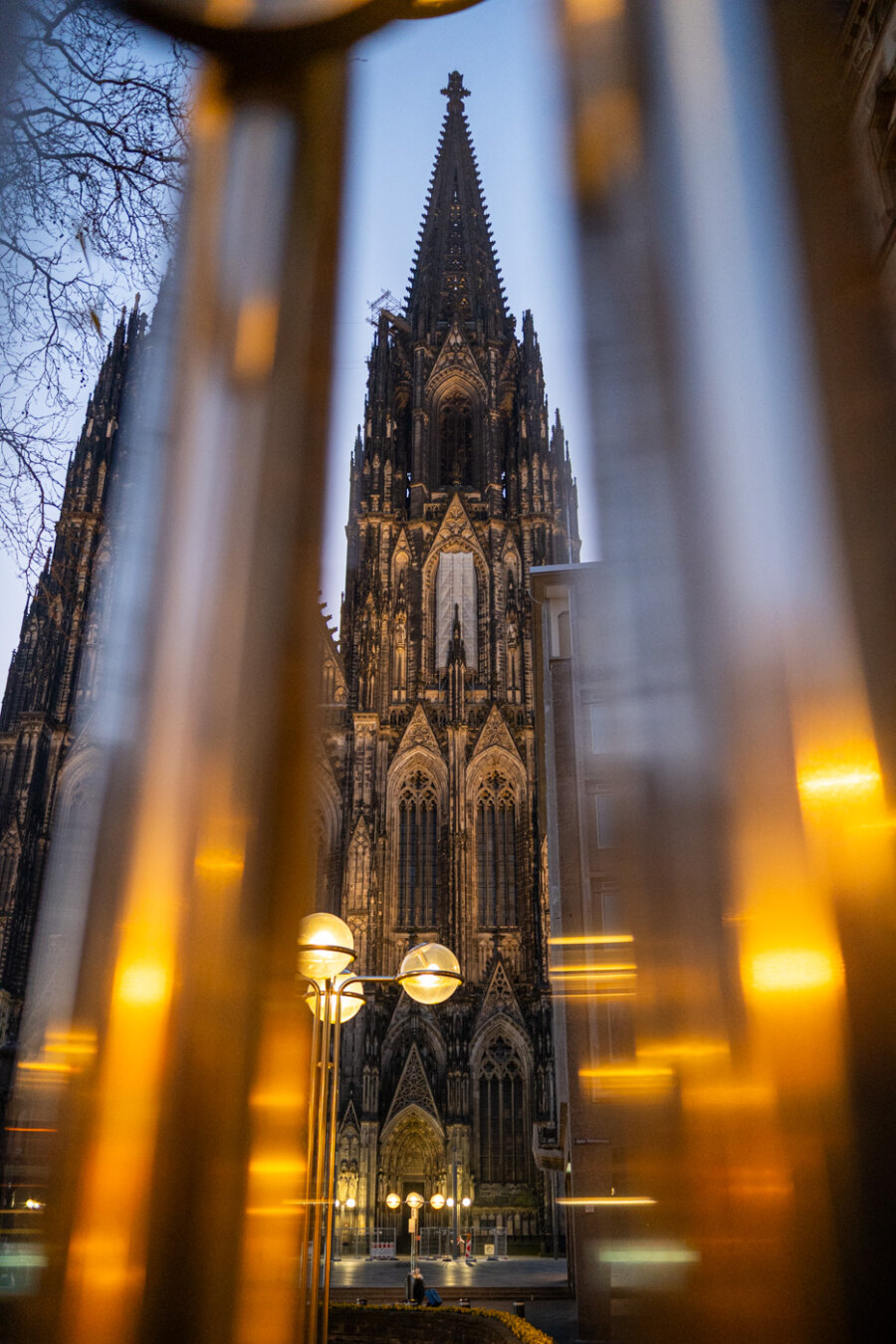 Ein Turm des Kölner Doms ist zu sehen, durch vergoldete Stäbe fotografiert auf denen sich entsprechende Reflexionen zeigen. Im Vordergrund sind noch Laternen sehen, mit jeweils 4 runden Lampen. Ein Turm des Kölner Doms ist zu sehen, durch vergoldete Stäbe fotografiert auf denen sich entsprechende Reflexionen zeigen. Im Vordergrund sind noch Laternen sehen, mit jeweils 4 runden Lampen.