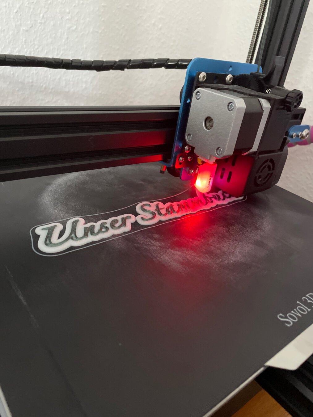 3D Printer actively printing a phrase in dark green on white filament
