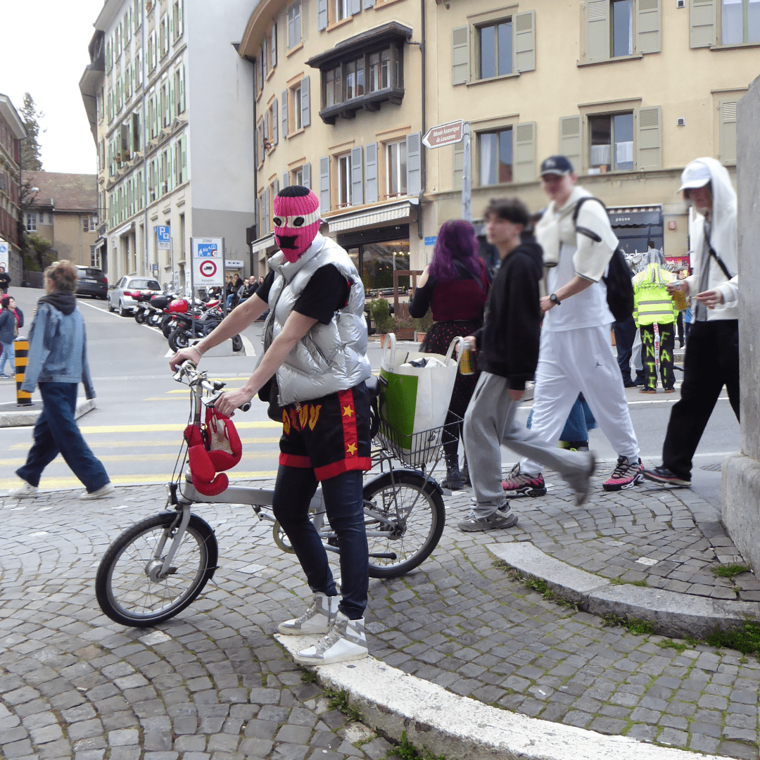 A person holding a grey folding bike wears a pink knitted mask and a silver down jacket