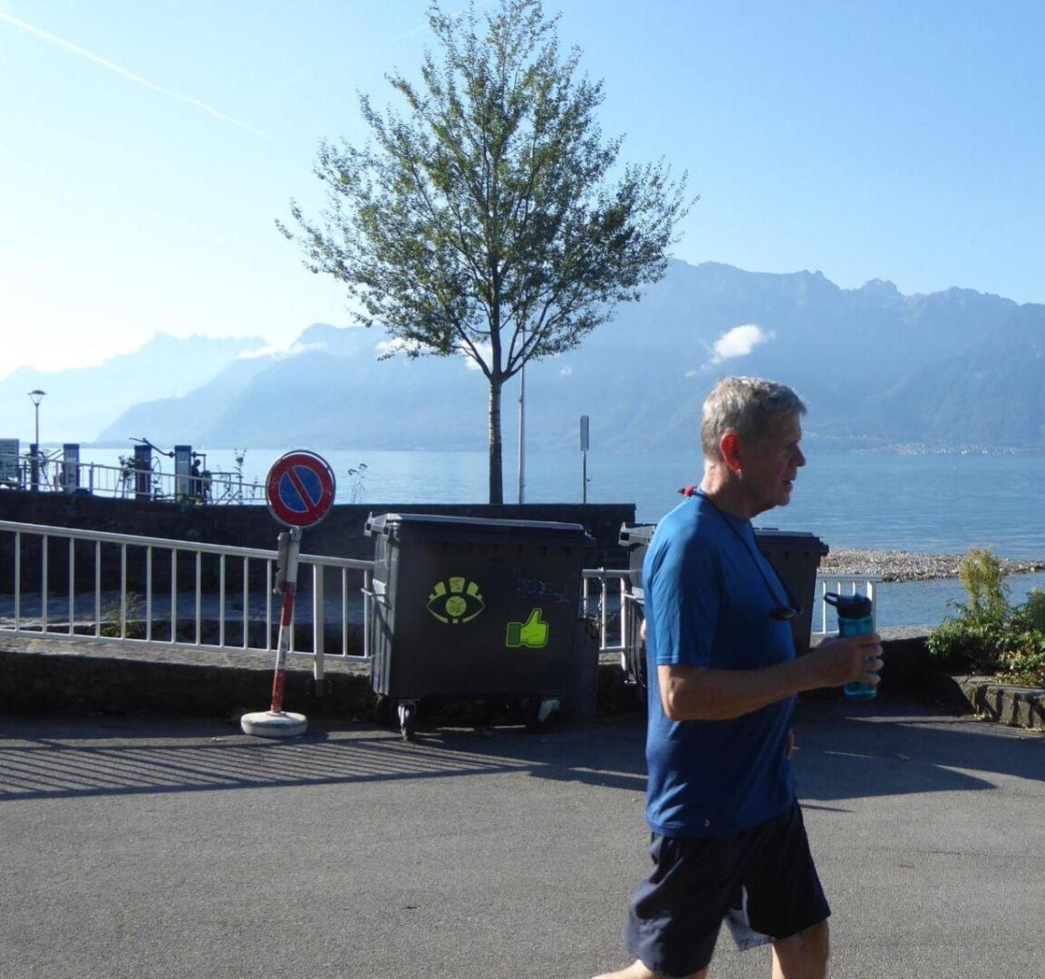 an image from my Pixelfed, shows an older man jogging in front of some garbage cans and the lac leman in Vevey for the Festivalk Images